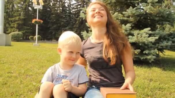 Jonge moeder met haar zoon in het park lezen van een boek op een wandeling — Stockvideo