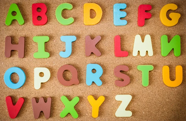 Alfabeto di legno colorato su tavola di sughero — Foto Stock