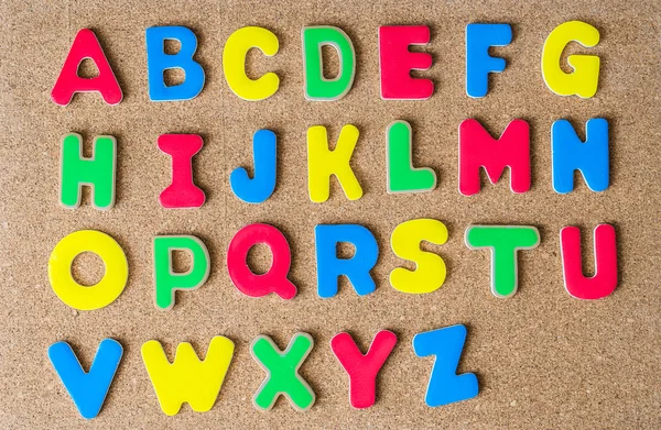 Alfabeto de letras mayúsculas de madera colorido en el tablero de corcho —  Fotos de Stock