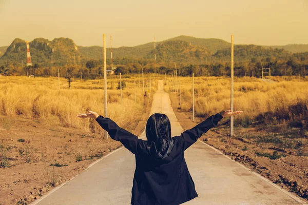 Hot temperature sunset scene in straight Countryside road with woman raise two hands up and dried meadow grass in two sides with clear blue sky for travel concept idea