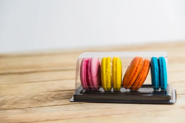 Kleurrijke macaron in plastic doos op houten vloer — Stockfoto