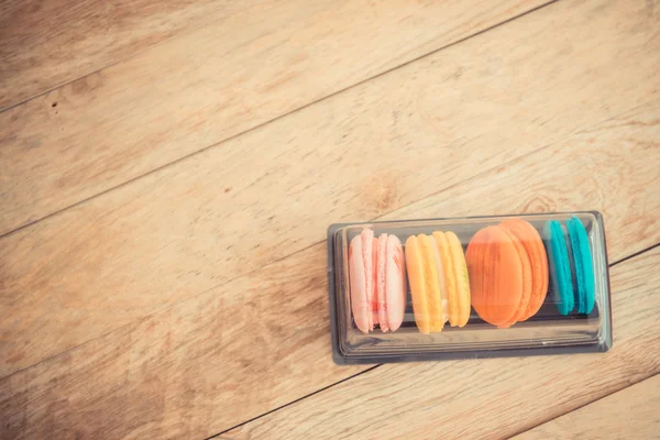 Kolorowy macaron w plastikowe pudełko na drewnianej podłodze w Vintage tematu — Zdjęcie stockowe