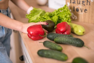 Genç bir kadın mutfakta taze sebze tutuyor..
