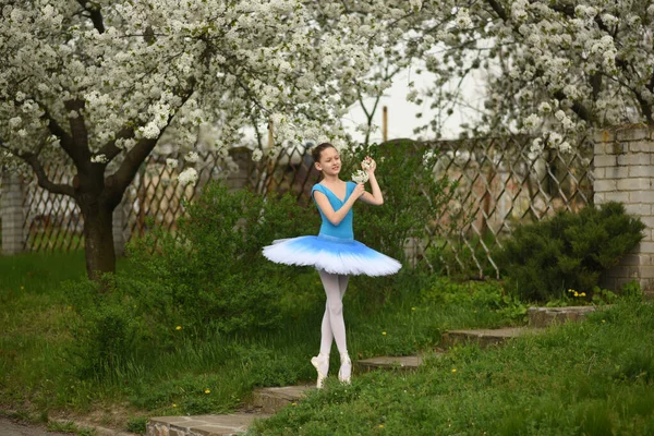 Ballerina in pointe shoes and a ballet tutu in the park. Ballet positions. Beautiful child in the park in spring in flowering trees