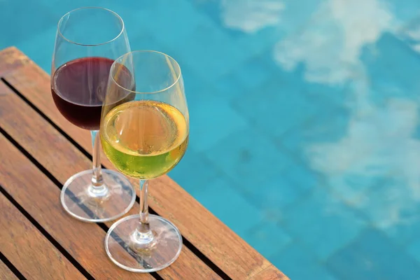 Yazın yüzme havuzunun yanındaki ahşap masada iki bardak şarap.