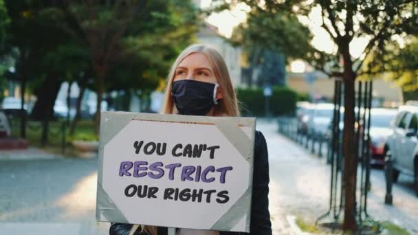 Ξανθιά γυναίκα που φοράει ιατρική μάσκα διαμαρτυρόμενη κατά του περιορισμού των ανθρωπίνων δικαιωμάτων — Αρχείο Βίντεο
