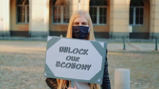 Молода жінка в медичній масці закликає розблокувати економіку, тримаючи пароплав — стокове відео