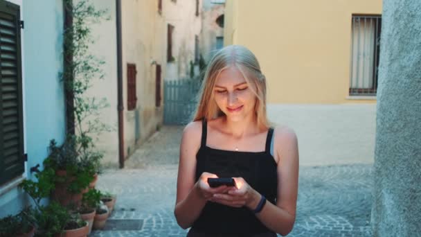 Beautiful young lady chatting on smartphone while walking on the street — Stock Video