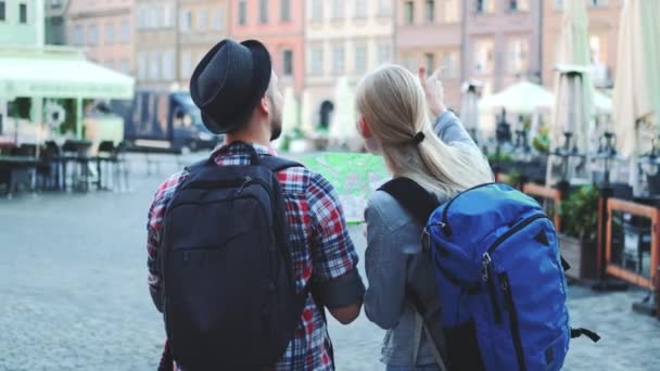 Tampilan belakang dari pasangan wisatawan dengan tas memeriksa peta di alun-alun Central City — Stok Video
