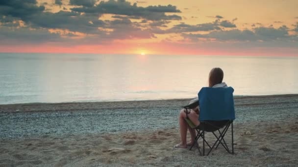 Mulher admirando pôr do sol no mar sentado em cadeira turística dobrável — Vídeo de Stock