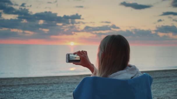 Mulher fazendo vídeo de pôr do sol com smartphone sentado na praia — Vídeo de Stock