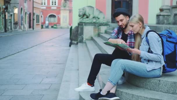 Turista pár ül az utcán lépcsőn, ellenőrzi a város térképét, és megvitatják — Stock videók