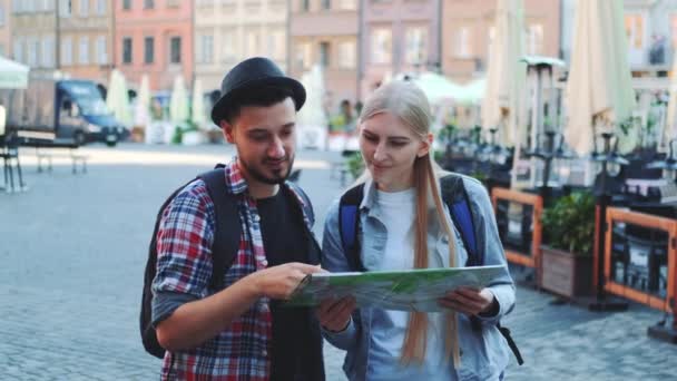 Счастливая молодая пара туристов проверяет карту, а затем улыбается камере — стоковое видео