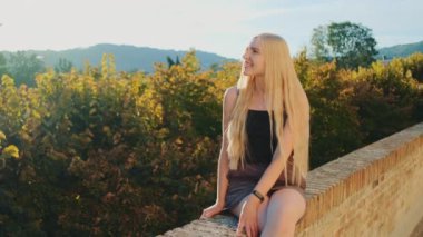 Sarışın kadın dinleniyor ve güneş ışığında gülümsüyor.