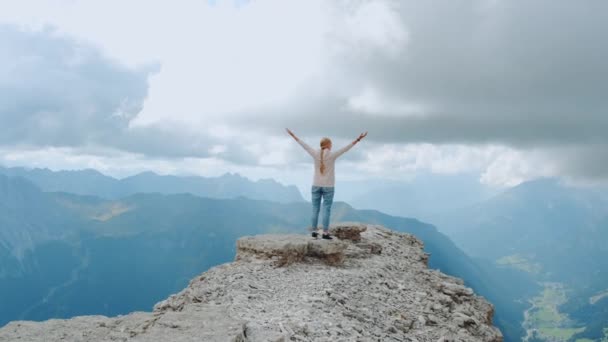 Jovem com braços estendidos apreciando a beleza da natureza na rocha da montanha — Vídeo de Stock