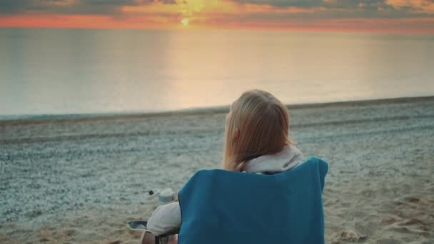 Woman drinking from thermal mug and sitting on the beach before sunrise — Stock Video