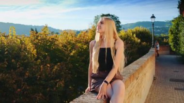 Sarışın kadın güneşlenip gülümsüyor.