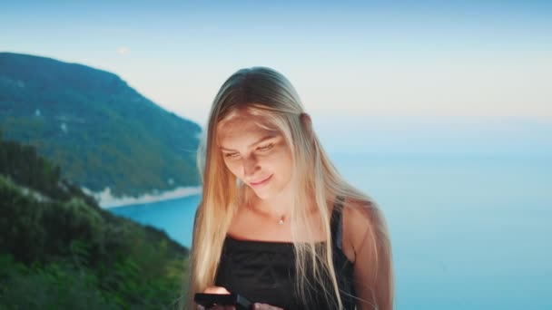 Arkasında okyanus olan akıllı telefon kullanan bir kadın. — Stok video