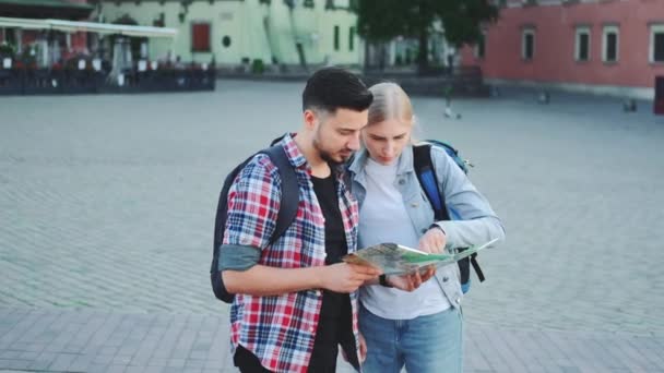 Man och kvinna håller karta och letar efter något ställe på torget — Stockvideo