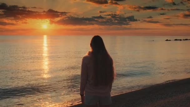 Mulher com braços estendidos apreciando a beleza do pôr do sol no mar — Vídeo de Stock