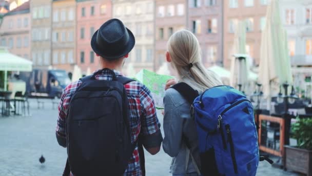 Hombre y mujer con bolsas chequeando mapa en la plaza central de la ciudad — Vídeos de Stock