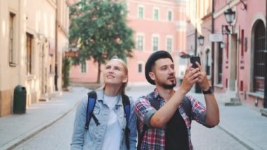 Genç turist çift sokakta yürüyor ve akıllı telefondan fotoğraf çekiyor.