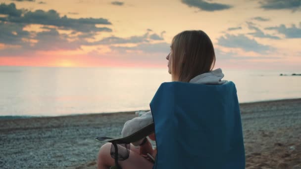 Mujer bebiendo del termo y sentada en sillas de camping en la playa — Vídeos de Stock