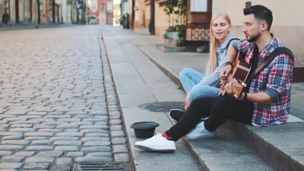 Jonge paar straatzangers in het oude deel van de stad zitten op de stoep — Stockvideo