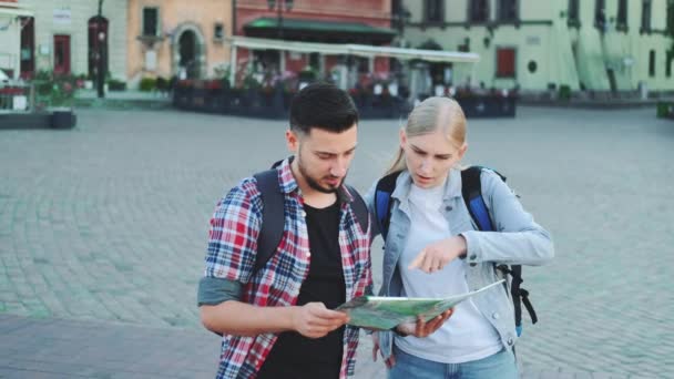 Un par de turistas sosteniendo el mapa y buscando un lugar en la plaza de la ciudad — Vídeos de Stock
