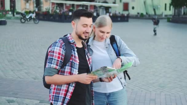 Туристы пара держит карту для поиска нового интересного места для осмотра достопримечательностей — стоковое видео