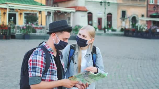 Twee toeristen in beschermende maskers met behulp van kaart op het centrale stadsplein — Stockvideo