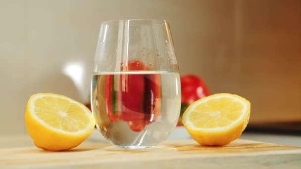 Sebuah gelas dengan air antara dua bagian lemon dipotong di papan dapur kayu — Stok Video