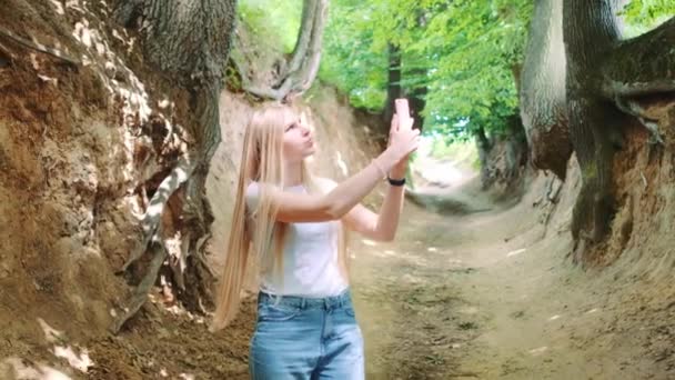 Blondýny mladá žena dělat fotografie na smartphone v magické kořeny rokle — Stock video