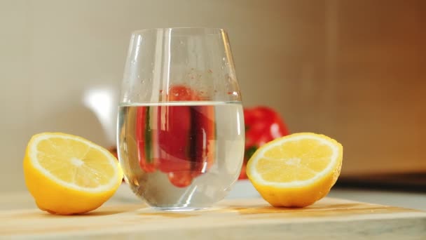 Ein Glas mit Wasser zwischen zwei Teilen geschnittener Zitrone auf hölzernem Küchenbrett — Stockvideo