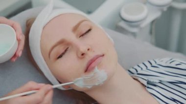 Güzellik salonunda genç kadınların yüzüne krem maske takan kozmetikçi elleri.