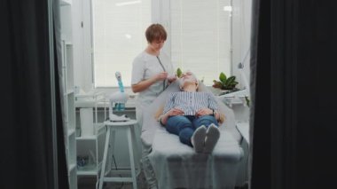 Güzellik salonunda güzel bir kadının yüzüne krem maske takan kozmetikçi.