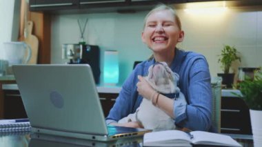 Gülümseyen kadın bilgisayarın başında oturmuş Bulldog 'u okşuyor ve sarılıyor.