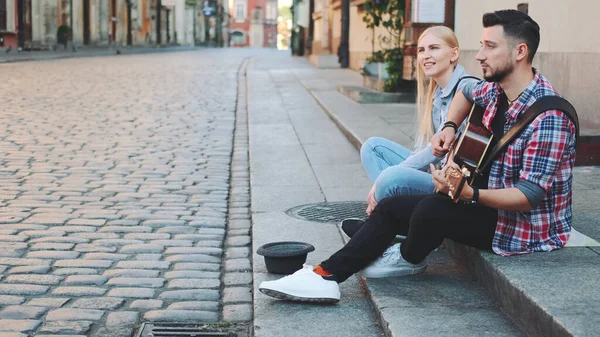 Casal jovem de cantores de rua na parte antiga da cidade sentado na calçada — Fotografia de Stock