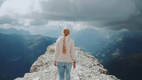 Vista posteriore della donna bionda che cammina sulla cima della montagna sotto le nuvole — Foto Stock