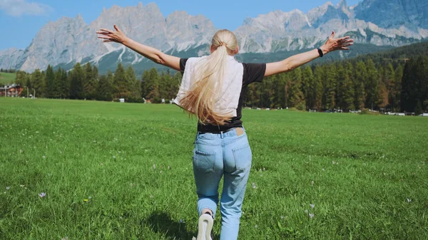 Vista posteriore della donna che corre sul campo con le montagne davanti — Foto Stock