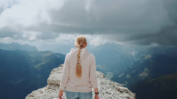 Zadní pohled na blondýny kráčející na vrcholu hory pod mraky — Stock fotografie