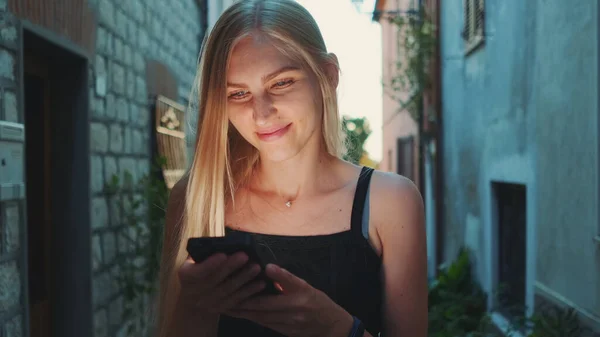 stock image Close-up of positive blonde woman reading something on smartphone while walking the street