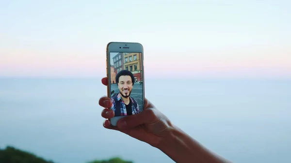 Main tenant smartphone lors d'un appel vidéo avec l'homme devant la mer — Photo