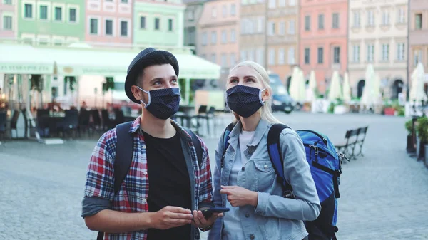 Man en vrouw in beschermende maskers en met tassen met smartphone — Stockfoto