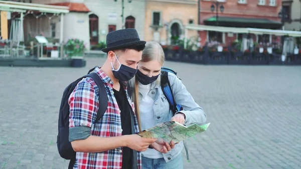 Two tourists in protective masks using map on central city square — Stock Photo, Image