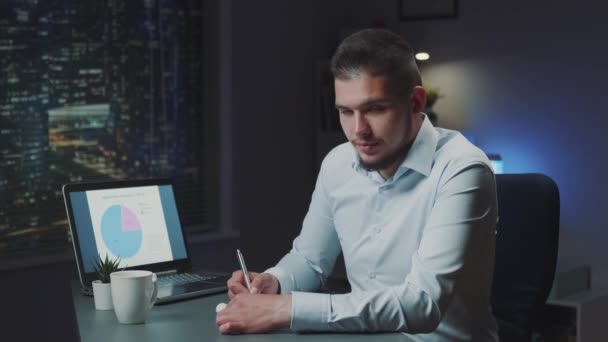 Bonito homem estudando até tarde da noite e sorrindo para a câmera — Vídeo de Stock