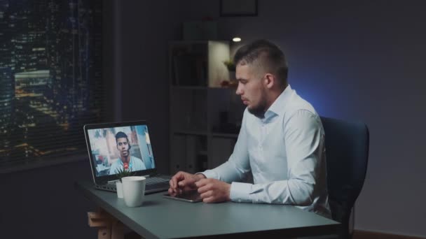 Videoconferencia ampliada con jefe de raza mixta en el ordenador tarde en la noche — Vídeos de Stock