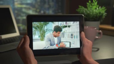 Tablet screen with video call: mixed-race man showing charts and explaining something