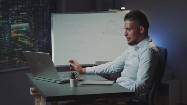 Fiatal latin férfi biztosít videokonferencia hívást számítógépen az irodában éjszaka — Stock videók