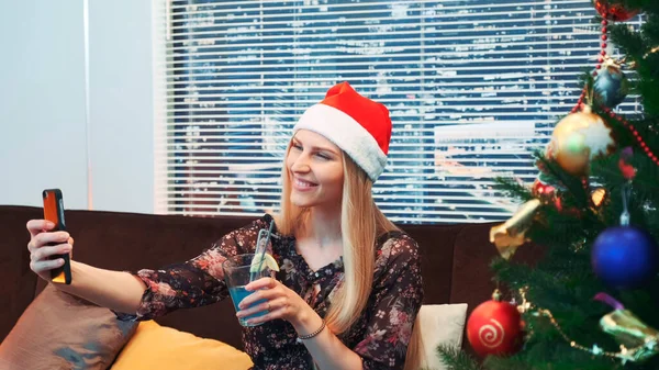 Vue latérale de belle femme faisant selfie dans le chapeau de Père Noël et avec boisson dans ses mains — Photo